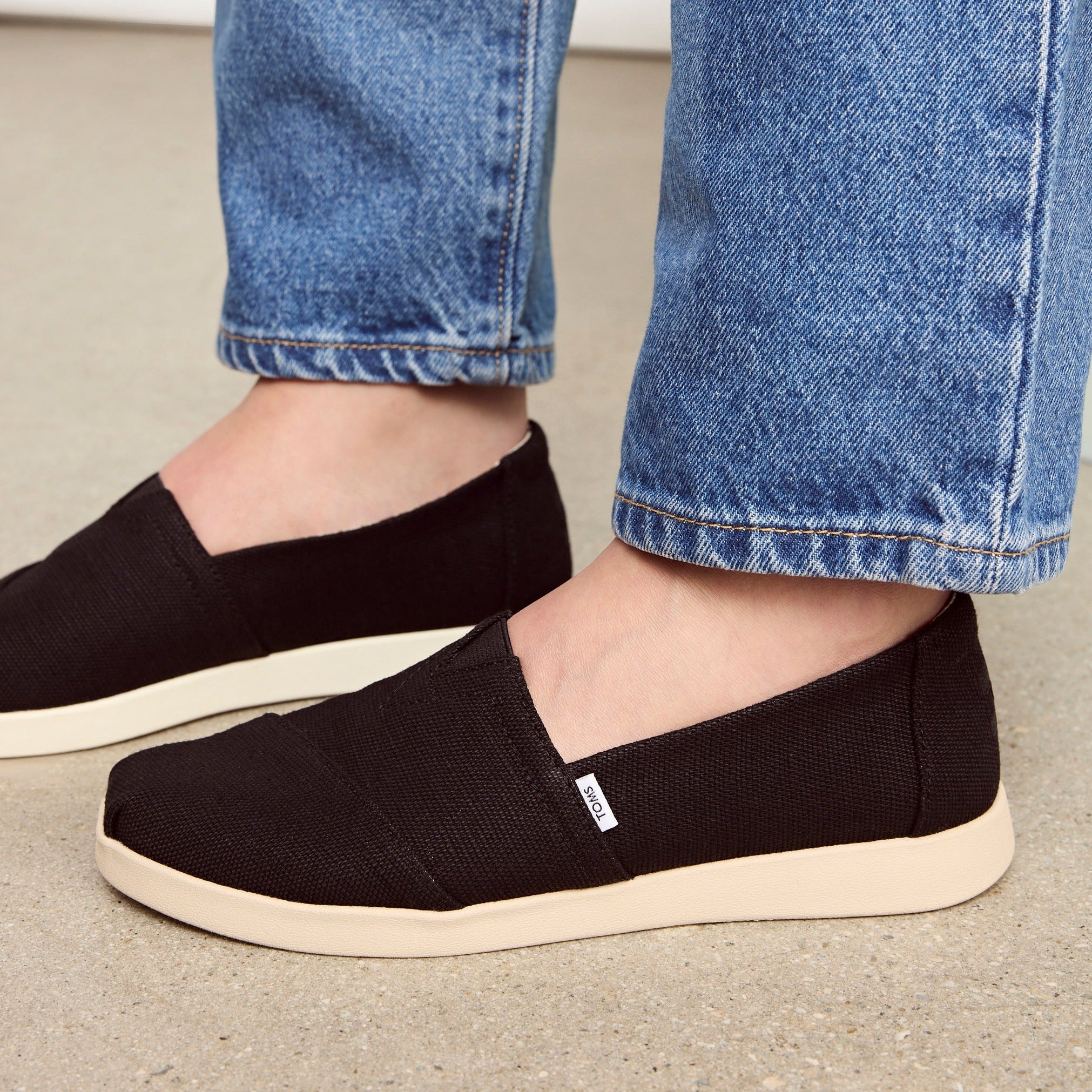 Up Close On Model Shot Of Alpargata Plus Slip On Casual Shoe In Black Canvas Styled With Denim Jeans